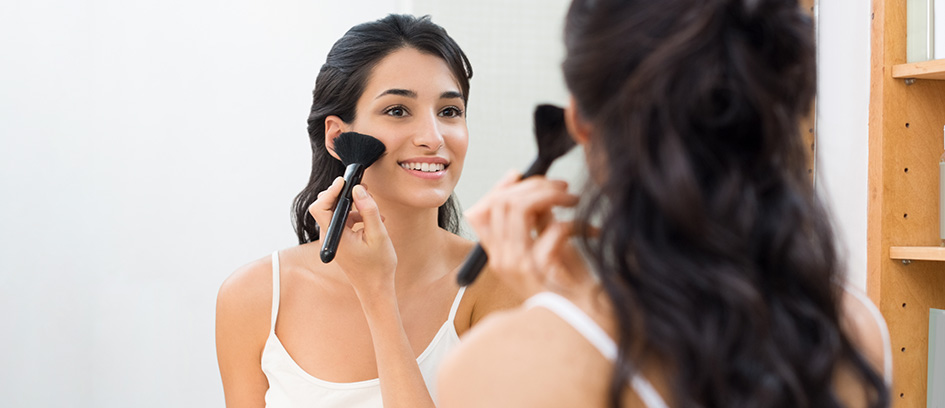 Woman applying makeup while looking in a mirror.