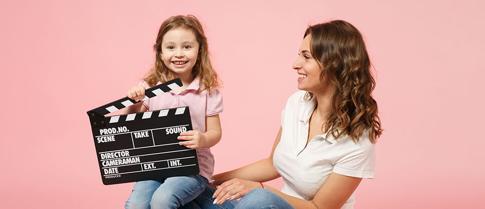 A mother and daughter with a clapper board on a pink background.