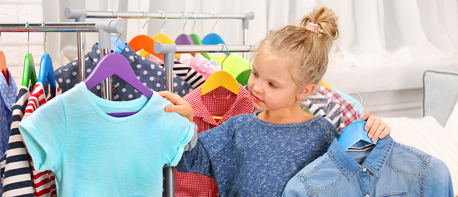 Young blonde girl holding up a blue dress and denim jacket.