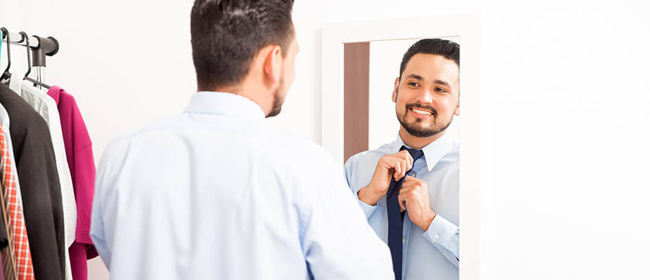 Man looking in mirror tying a tie.