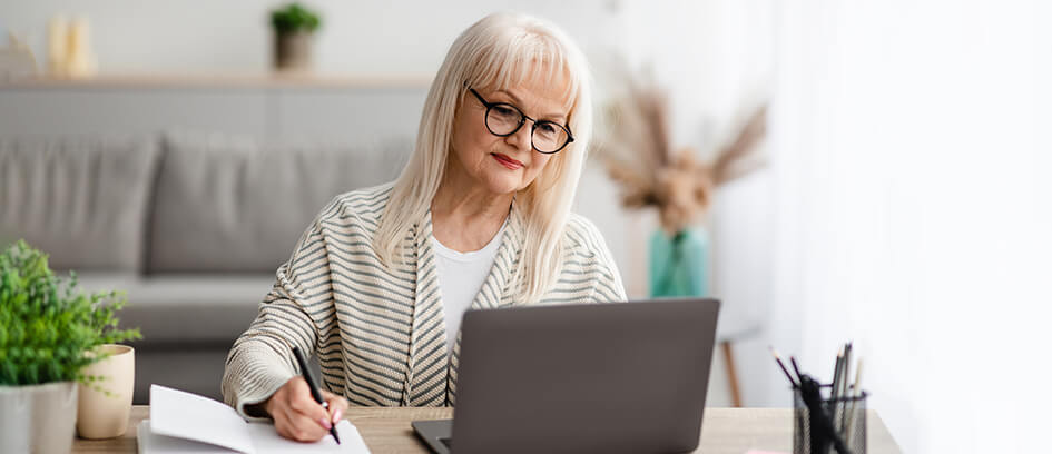 Woman taking notes and watching Virtual Visiting on a laptop.